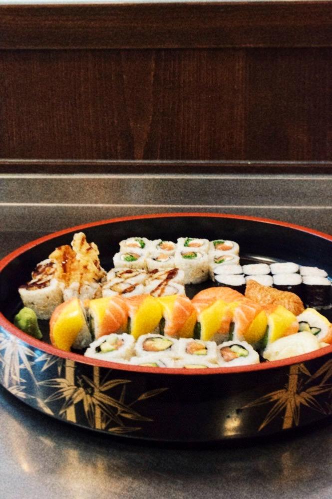 Platte mit verschiedenen Sushi-Rollen, serviert in einer traditionellen schwarz-roten Schale im japanischen Stil mit Bambusmuster.