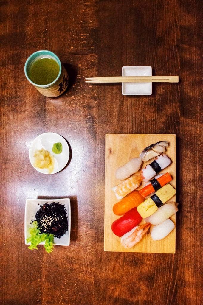 Draufsicht auf eine Sushi-Mahlzeit mit verschiedenen Nigiri, einer Tasse grünem Tee, Seetangsalat, eingelegtem Ingwer und Wasabi, serviert auf einem Holztisch.